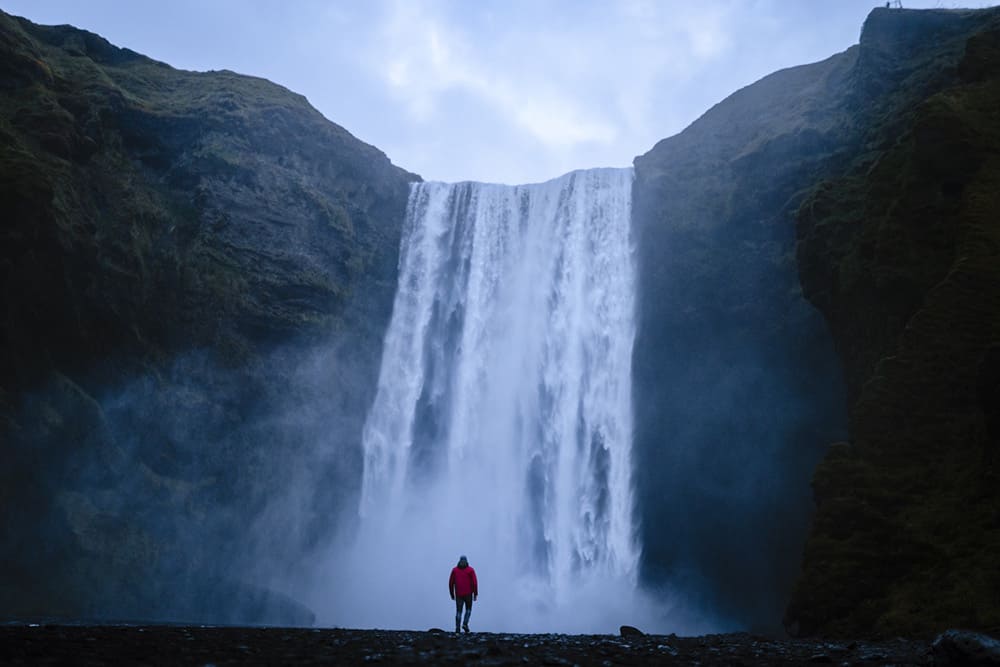 hombre frente a una cascada en la montaña
